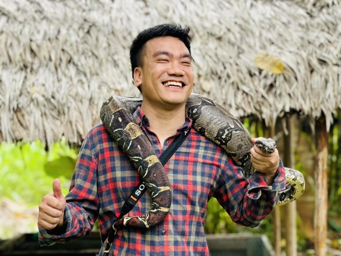Anh Hiếu khoác trăn đỏ lên vai khi đến rừng Amazon. Trăn xanh anaconda được nuôi trong chuồng phía sau chỗ anh Hiếu đứng.